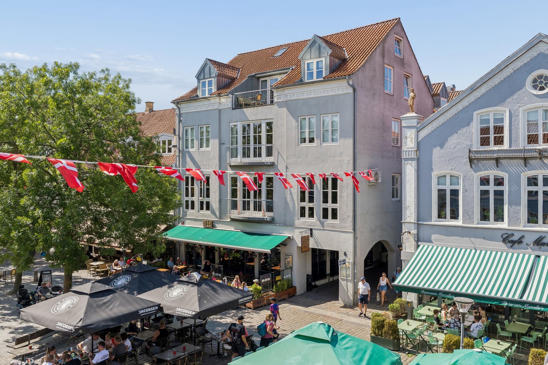 Rådhustorvet 6 i Sønderborg med lysegrå facade, kviste, balkoner og grøn markise
